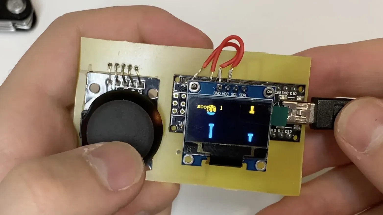 Handmade yellow PCB holding an analog joystick, OLED, and Arduino Nano while running FlappyZavr